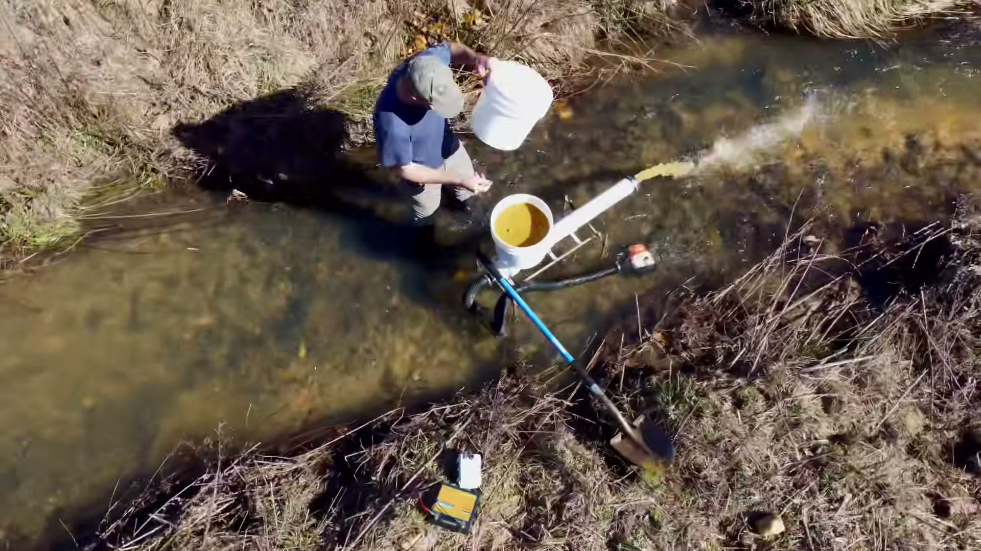 Aerial view of the builder shoveling gravel into the sluice bucket in a shallow stream